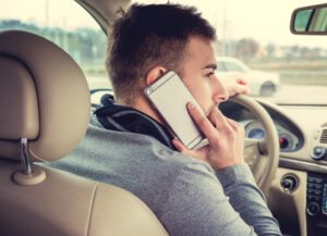 Homem dirigindo carro enquanto fala ao telefone celular, foco na atenção na segurança ao usar o telefone ao volante.