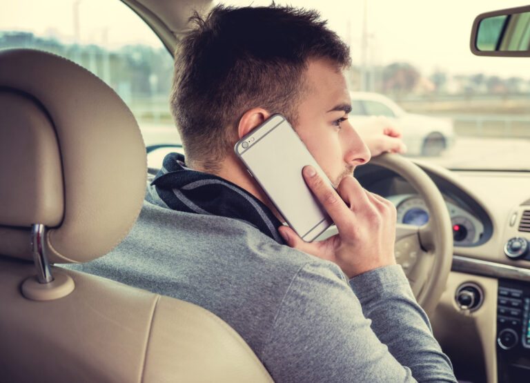 Homem dirigindo carro enquanto fala ao telefone celular, foco na atenção na segurança ao usar o telefone ao volante.